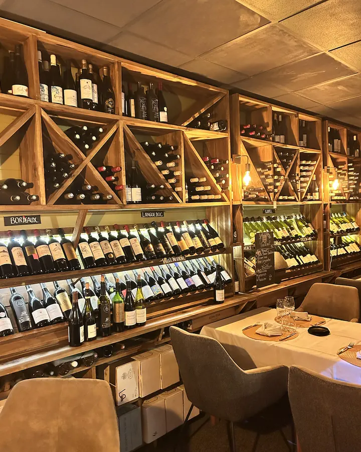 La salle en cave : un mur de casiers à vin en bois blond, des tables nappées de blanc