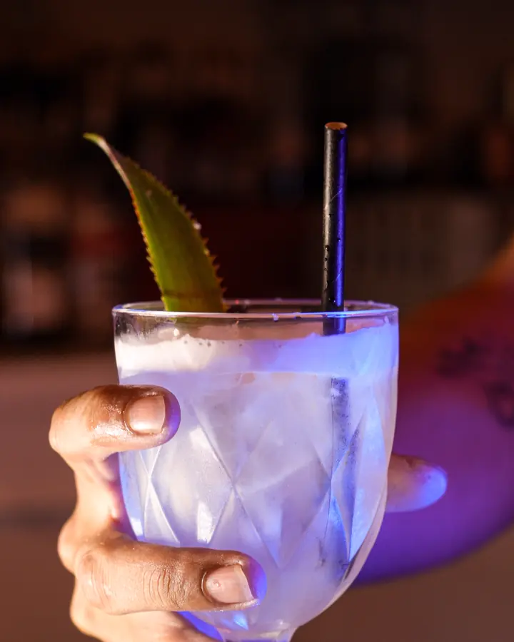 Une Piña Colada clarifiée servie dans un verre taillé, avec une feuille d'ananas
